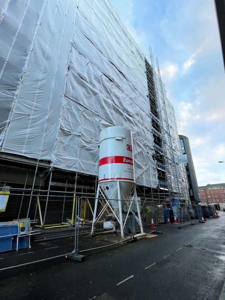 concrete mixer in front of plastic covered scaffolded building