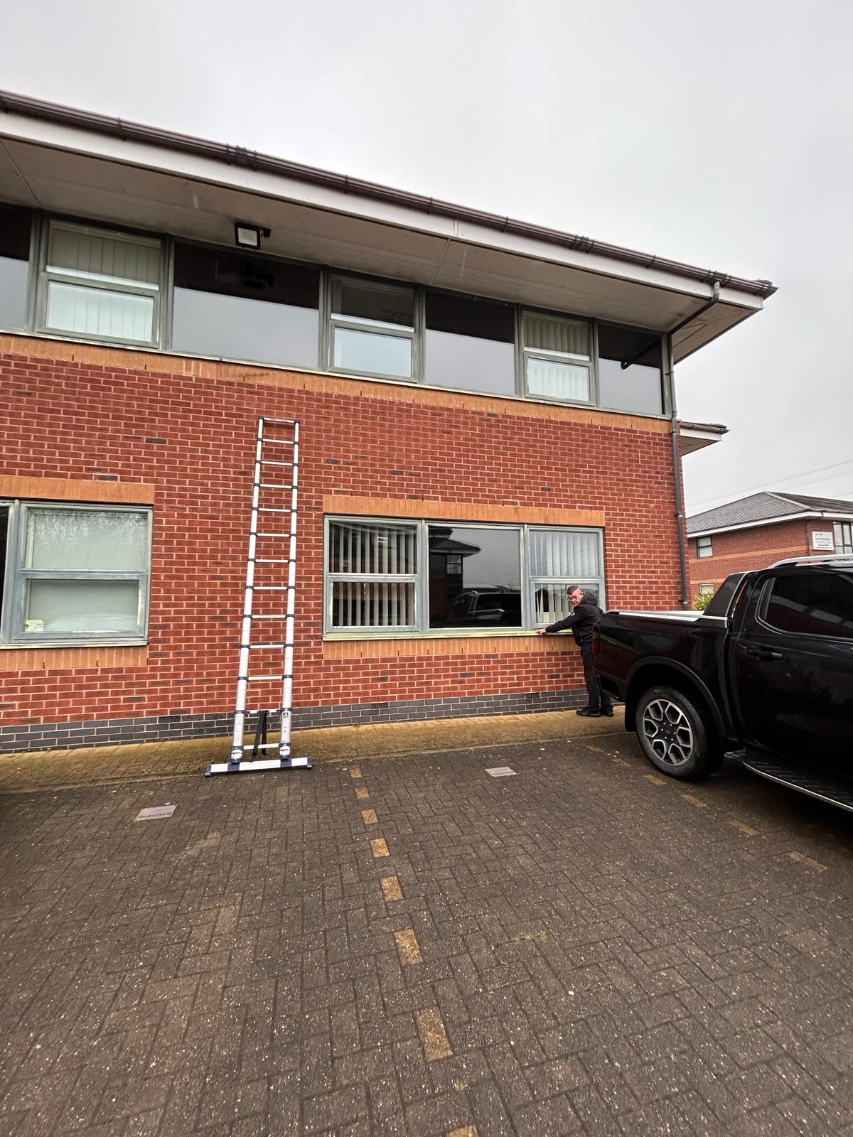 Ladder leaning against a red brick building with lots of glass windows incorporated below the roofline